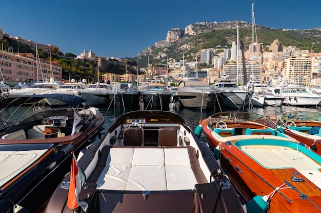 Un montón de barcos a motor en filas están en el puerto de mónaco en un día soleado la montaña de monte carlo está en el fondo...