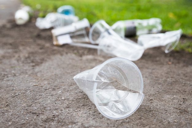 Montón de basura en el camino, primer plano. Vasos de plástico usados vacíos y botellas de plástico