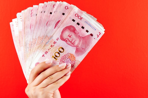 Un montón de billetes de RMB de yuan chino en una mano femenina en un rojo
