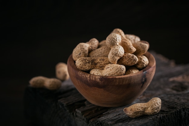 Montón de cacahuetes en un recipiente sobre una superficie de madera oscura.