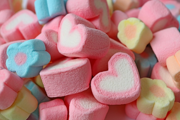 Montón de caramelos de malvavisco en forma de flor de color rosa y blanco en forma de corazón y pastel