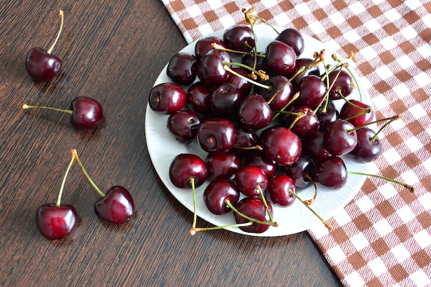 montón de cerezas de jardín en un plato blanco en la mesa de la cocina con mantel a cuadros