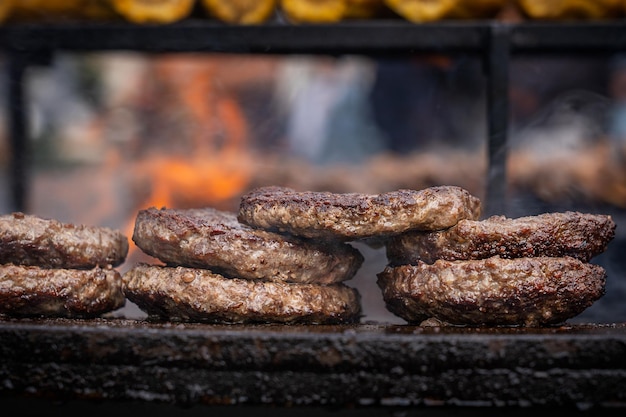 Un montón de chuletas o empanadas de carne picada sobre una parrilla al aire libre cocinada con llamas