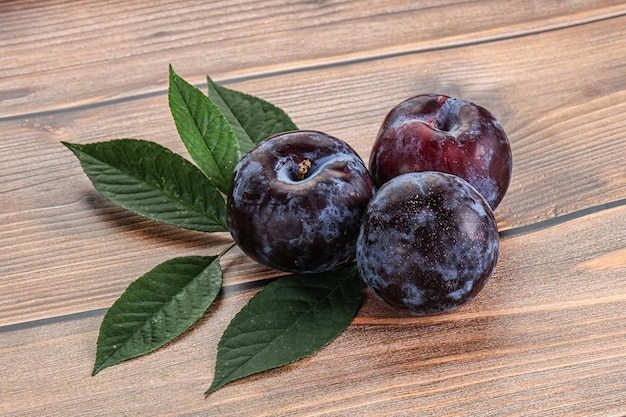 Un montón de ciruelas moradas crudas con hojas