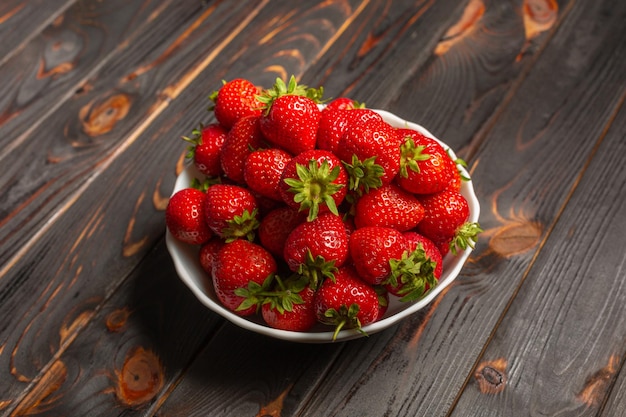 Un montón de fresas frescas en un cuenco de cerámica sobre un fondo de madera rústica