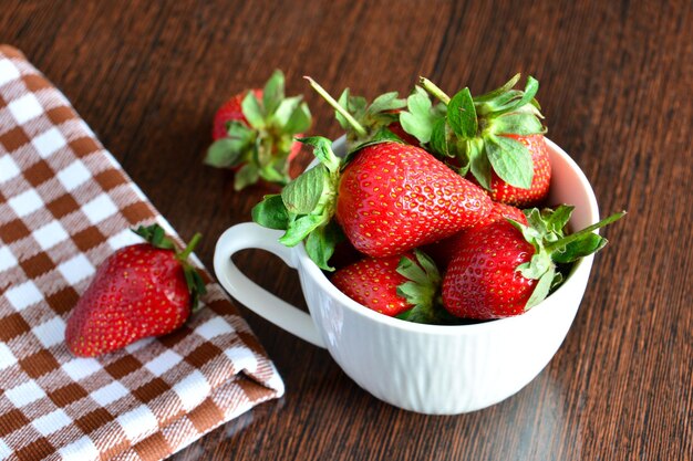 montón de fresas frescas en taza sobre fondo de madera, primer plano