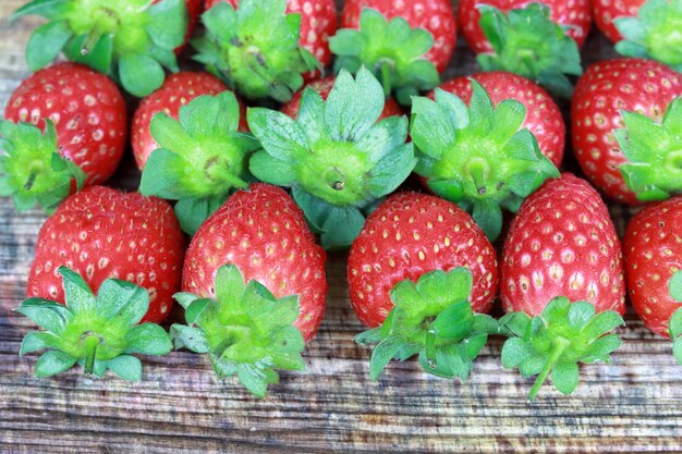 Un montón de fresas con hojas verdes sobre una superficie de madera.