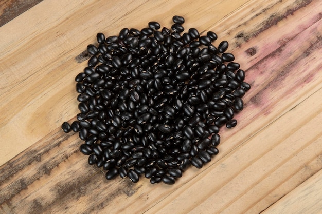 Foto montón de frijoles negros esparcidos sobre madera rústica