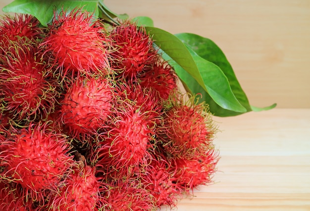 Montón de frutas frescas maduras de rambután con hojas verdes en la mesa de madera