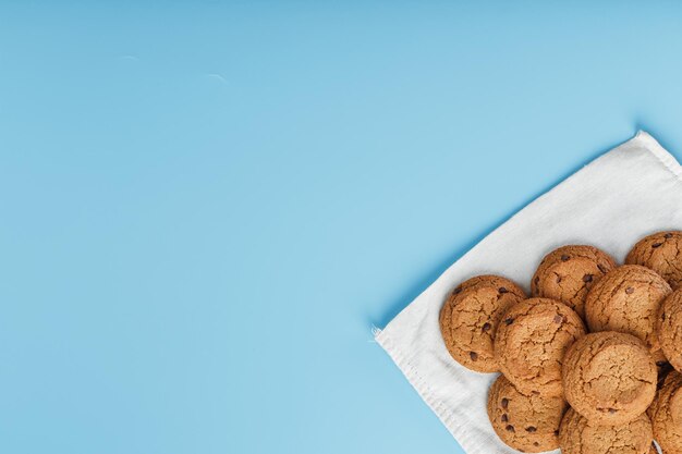 Un montón de galletas de avena con chocolate en una servilleta sobre un fondo azul. Vista superior, espacio libre.