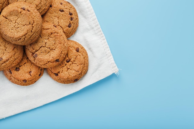 Un montón de galletas de avena con chocolate en una servilleta sobre un fondo azul.