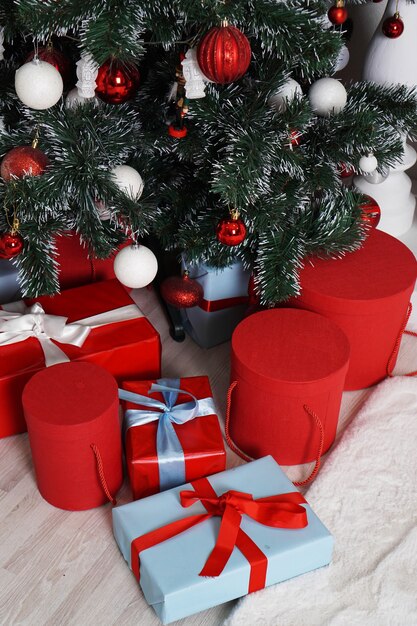 Un montón de hermosos regalos de Navidad envueltos en cajas redondas en rojo y azul debajo del árbol de Navidad.