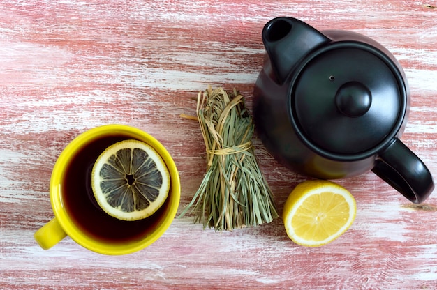 Un montón de hierba de limón seco, limón fresco, tetera y una taza de té.