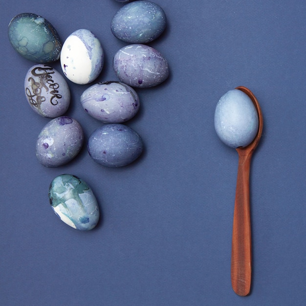 Un montón de huevos de Pascua y una cuchara de madera con un huevo azul sobre un fondo azul, plano laical