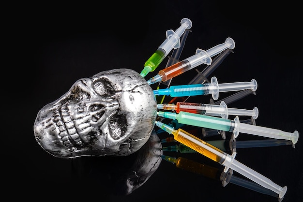 Montón de jeringas coloridas pegadas en cráneo metálico sobre sobredosis de drogas de fondo negro y estafa de muerte