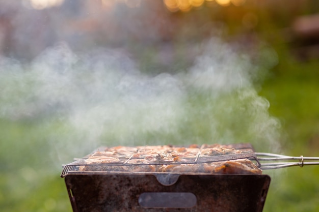 Foto un montón de jugosos kebabs de carne seguidos a la parrilla. trozos de carne ensartados en brochetas de metal a la parrilla al atardecer. el proceso de cocinar kebabs con mucho humo. cocinar en la naturaleza