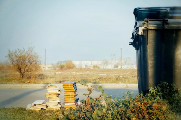 Foto un montón de libros viejos tendidos por la carretera cerca del contenedor de basura de plástico negro