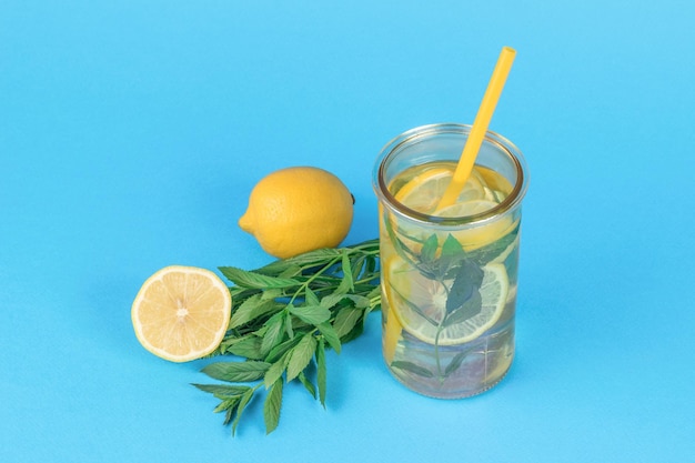 Un montón de limón de menta y un vaso de agua sobre un fondo azul.