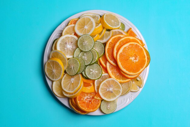 Montón de limones en rodajas, limas y frutas naranjas en un plato aislado de fondo azul