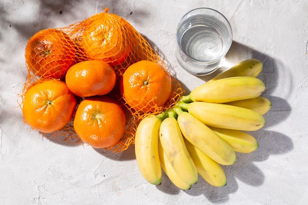 Montón de mandarinas frescas, plátanos y vidrio con agua en la mesa de hormigón