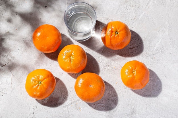 Montón de mandarinas frescas y vaso con agua sobre la mesa de hormigón