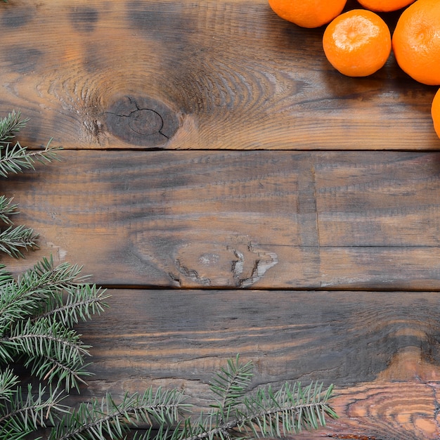 Un montón de mandarinas naranjas y ramas de abeto navideño yacen sobre tablones de madera marrón