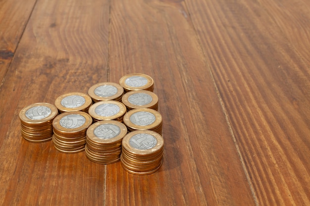 Un montón con un montón de monedas de dinero real brasileño apiladas sobre una mesa de madera