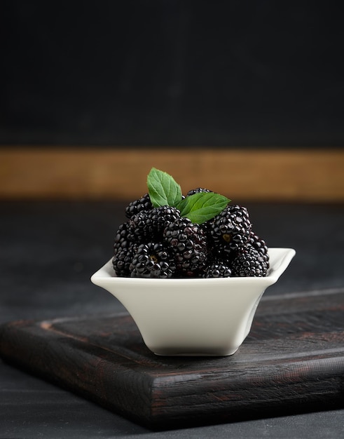 Un montón de moras maduras en un plato de cerámica blanca sobre una mesa negra