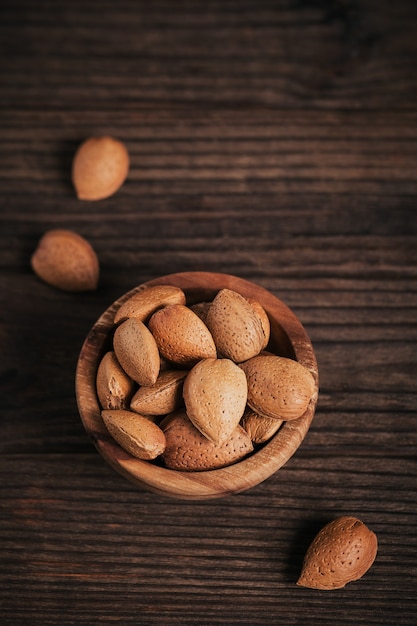 Montón de nueces de almendra en un recipiente sobre una superficie de madera oscura.