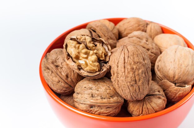 Montón de nueces en un recipiente naranja sobre un fondo blanco.