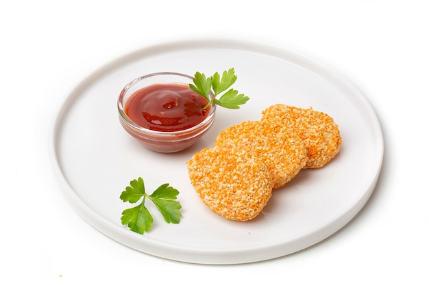 Un montón de nuggets de pollo cocidos en un plato con salsa de tomate, aislado sobre un fondo blanco.