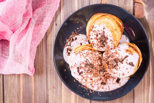 Foto un montón de panqueques rellenos de yogur de frutas y espolvoreado con chocolate rallado en un plato sobre una mesa de madera