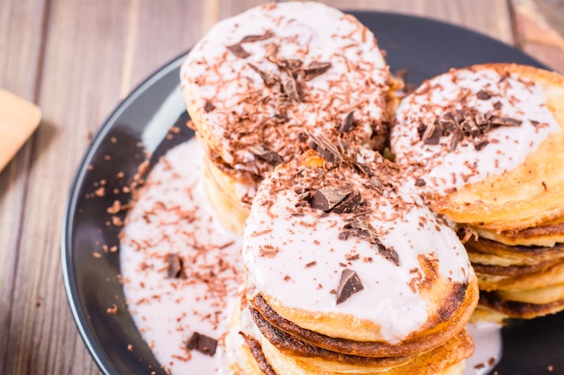 Un montón de panqueques rellenos de yogur de frutas y espolvoreado con chocolate rallado en un plato sobre una mesa de madera