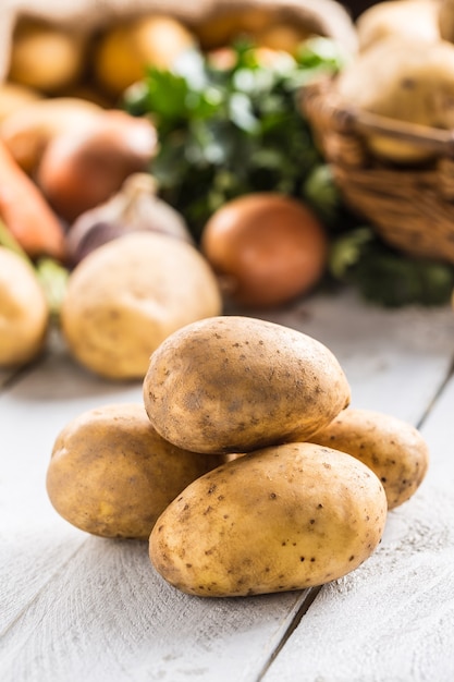 Un montón de patatas frescas y surtido de verduras en el fondo.