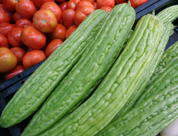 Montón de pepino amargo verde vibrante o pera bálsamo con canasta de tomates en el telón de fondo