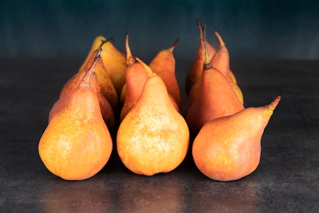 Un montón de peras naranjas de la cosecha de otoño sobre una mesa de piedra oscura.