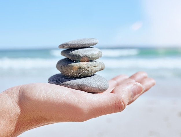 Montón de piedras de mano y playa con una mujer sosteniendo pequeñas rocas junto al océano para equilibrar el bienestar o el zen Naturaleza tierra y atención plena con una roca en la palma de una mujer en la arena junto al mar