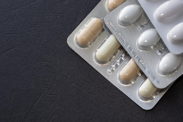 Montón de píldoras médicas en tabletas blancas, verdes y amarillas en paquete de plástico sobre fondo oscuro
