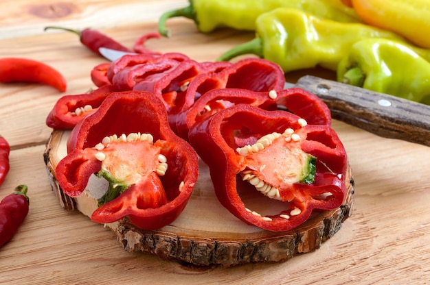 Un montón de pimientos enteros y picados en una mesa de madera Pimientos rojo naranja verde picante