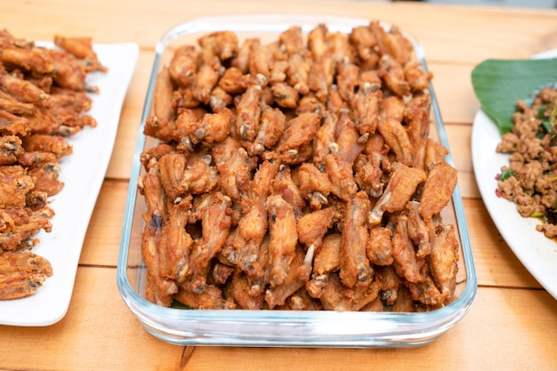 Un montón de pollo frito con alas pequeñas está dispuesto en el plato rectangular de vidrio en la mesa de mostrador de madera del almuerzo de los asiáticos