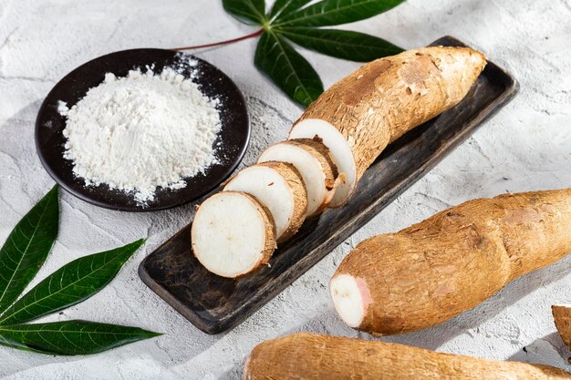 Montón de raíz de yuca y harina de yuca sobre un fondo de textura gris y blanco Manihot esculenta