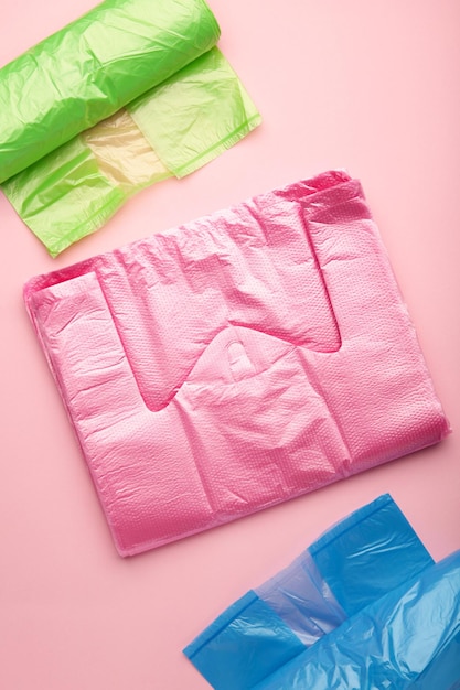 Un montón de rollos de bolsas de plástico de colores sobre un fondo rosa Foto vertical