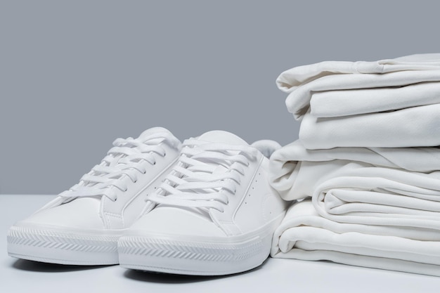 Un montón de ropa blanca y zapatillas con estilo sobre fondo gris