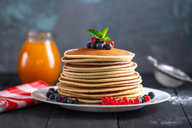 Montón de sabrosos panqueques caseros con bayas frescas y tarro de miel para un delicioso desayuno