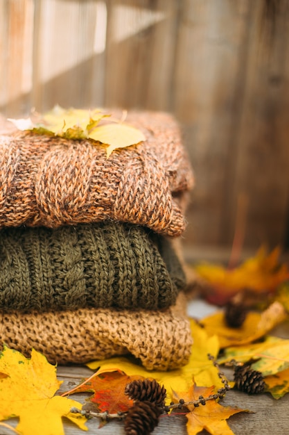 Un montón de suéteres calientes en una mesa de madera con hojas de otoño, prendas de punto, espacio para texto, concepto de otoño invierno.
