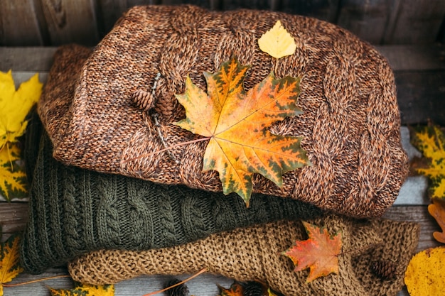 Un montón de suéteres calientes en una mesa de madera con hojas de otoño