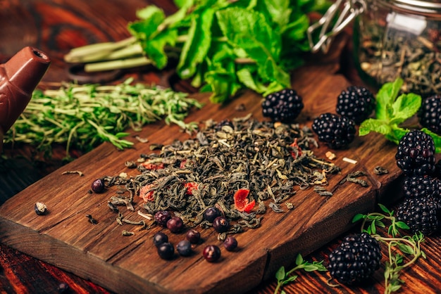 Montón de té verde seco y moras frescas sobre tabla de cortar de madera