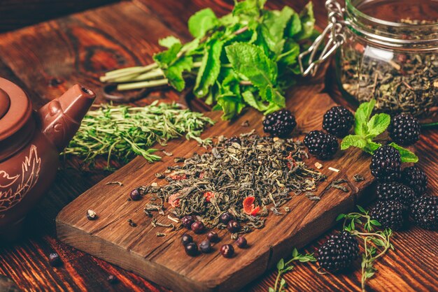 Montón de té verde seco y moras frescas sobre tabla de cortar de madera.