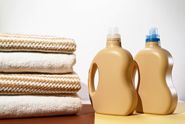 Montón de toallas de algodón y botellas de detergente líquido para lavar sobre fondo beige, hogar ecológico