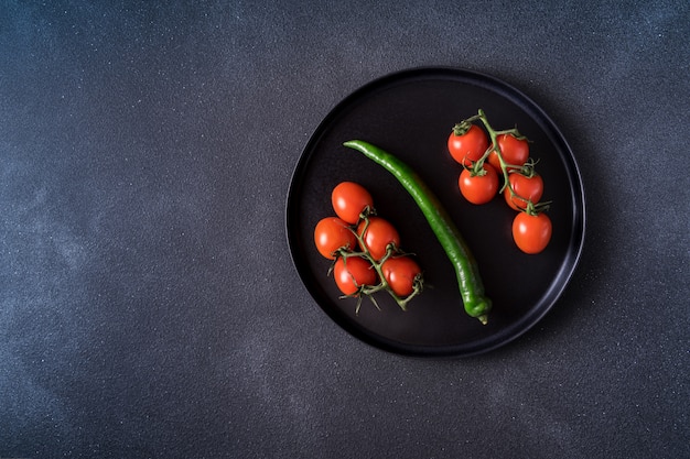 Montón de tomate cherry rojo y pimiento verde servido en plato negro sobre mesa negra